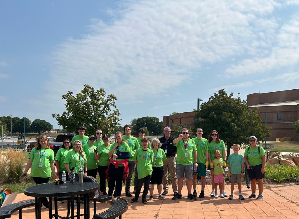 A large group of volunteers pose for a wide photo outdoors near a patio table.