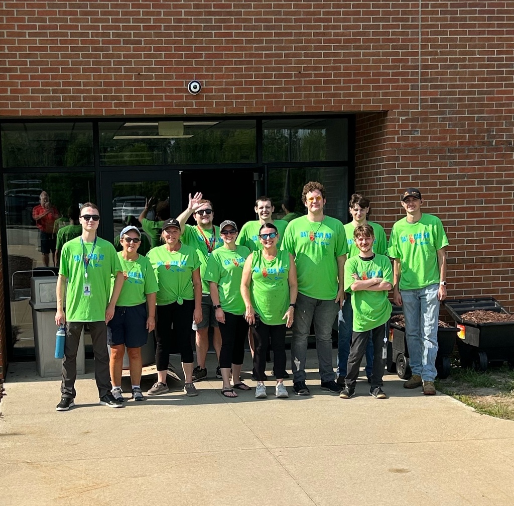 A group of volunteers in green t-shirts pose together outside a school entrance.