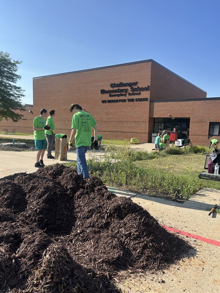 olunteers in green shirts spread mulch near a large pile outside Challenger Elementary School.