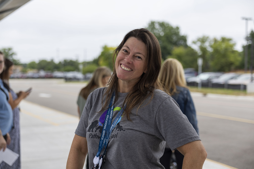 A woman in a grey Pathway School t-shirt smiles for a candid portrait outside.