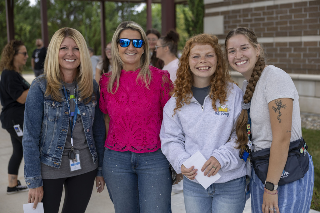 Four women pose together outdoors smiling for a group photo on the first day of school.