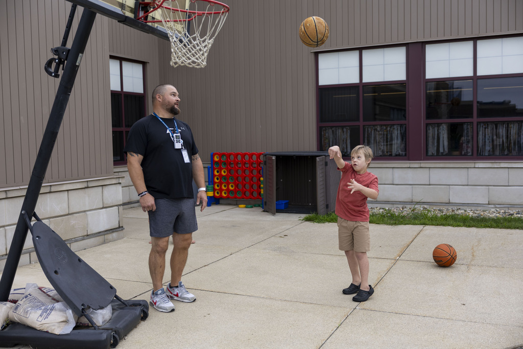 A young boy shoots a basketball toward a hoop while an instructor watches.