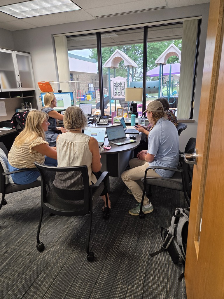 Five adults sitting around desk working on their computers.