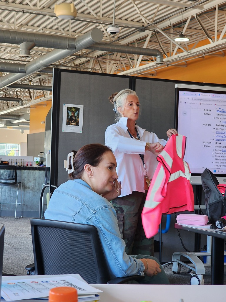 One female standing, leading a training session with one female sitting in a chair.