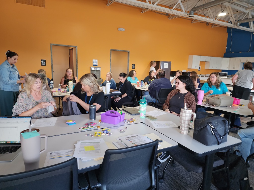 Female teachers sitting along tables, socializing.