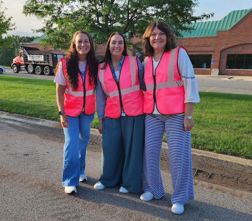 Three ladies standing in the road wearing pink constrution vests.