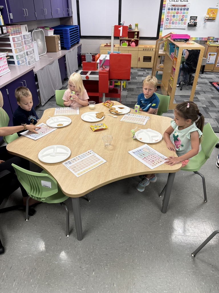 GSRP students eat breakfast together at a classroom table with individual mobile COR communication boards placed in front of them.