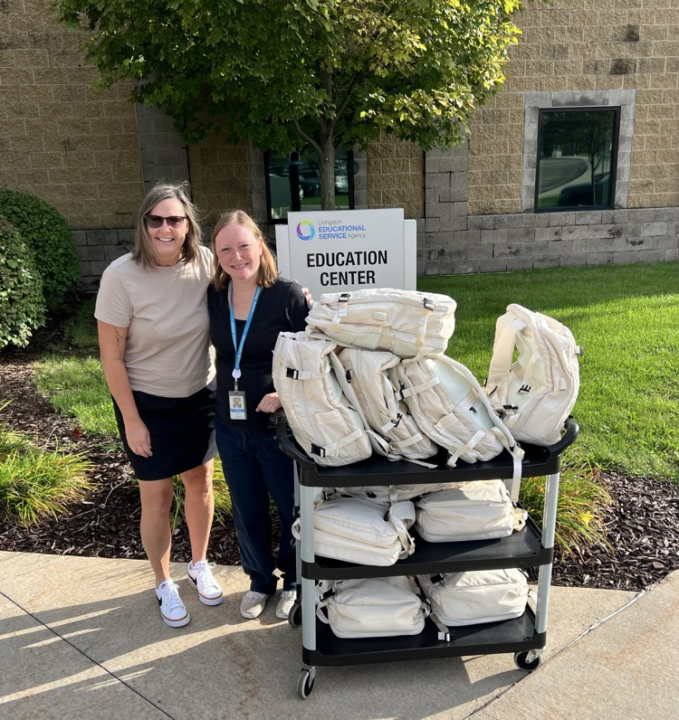 Two women standing next to a cart filled with backpacks. 