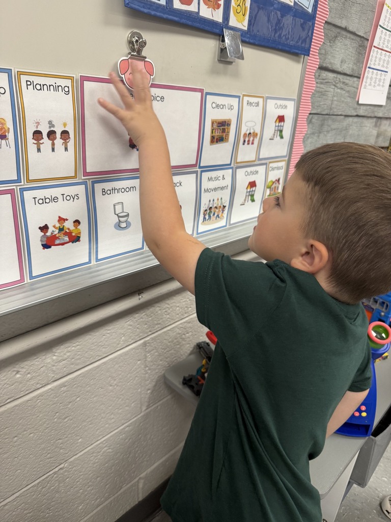 Preschooler reaches toward a classroom visual schedule to check the next activity in the daily routine.