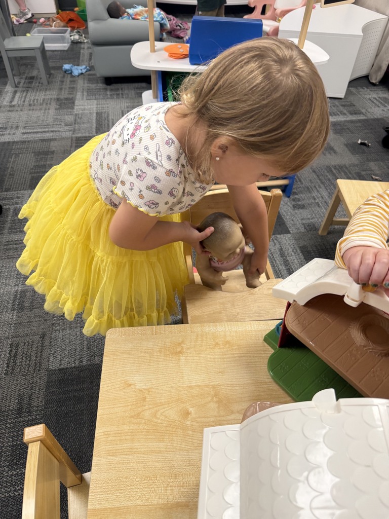Preschooler engages in pretend play, caring for a baby doll in the classroom dramatic play area.