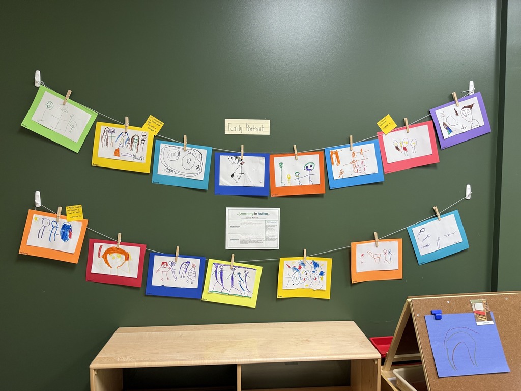 Children’s colorful family portrait drawings displayed on classroom walls at child eye level.