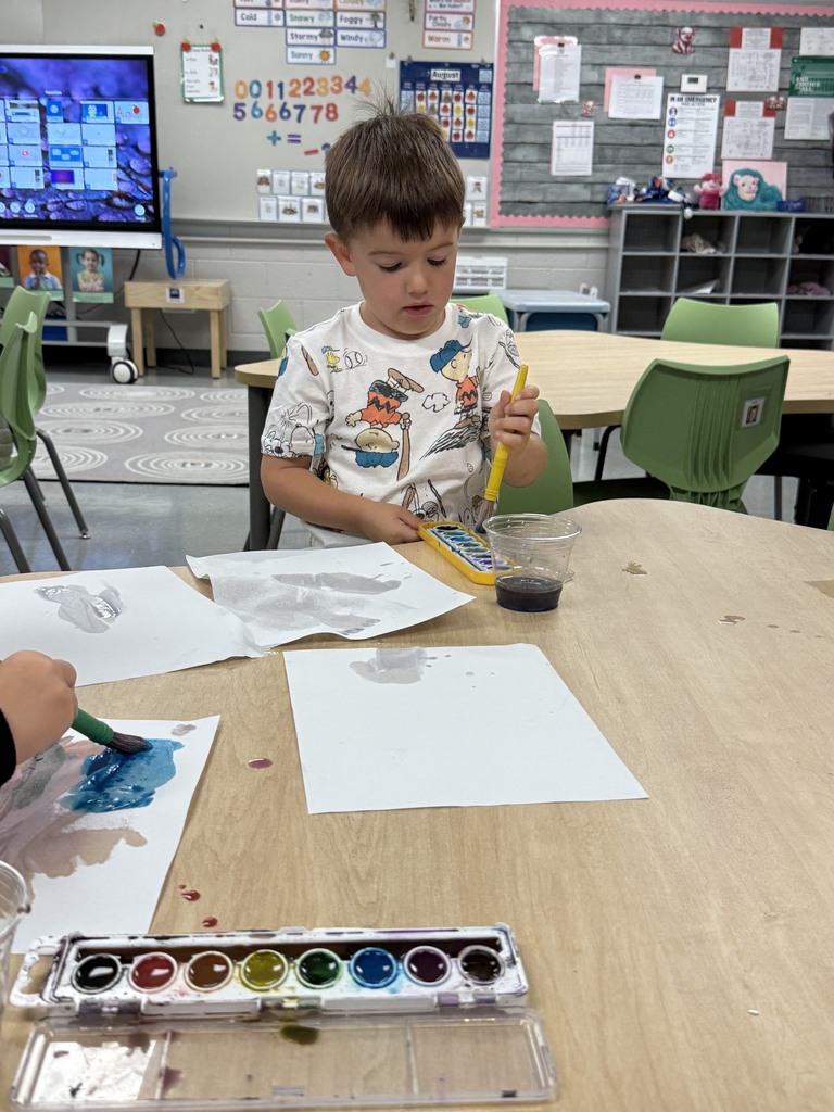 Preschooler uses watercolors and a paintbrush to create artwork during an open-ended classroom art experience.
