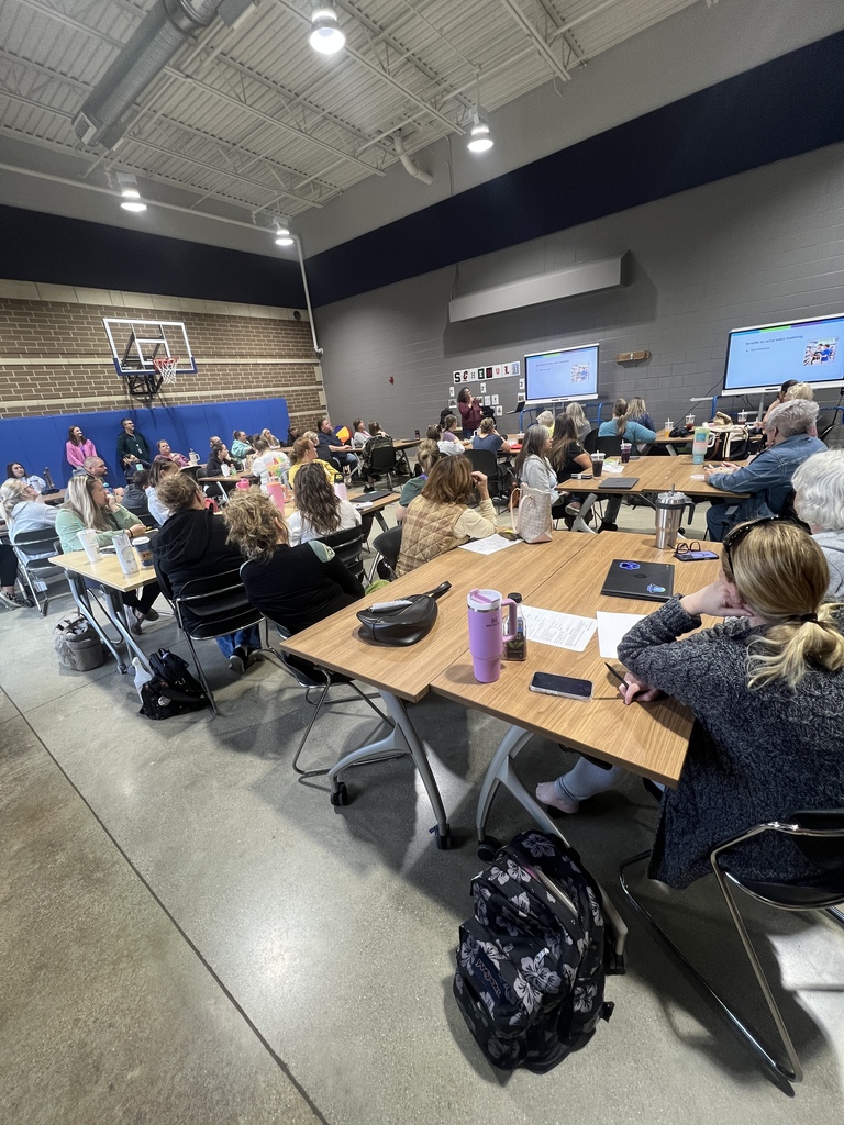 Wide shot of attendees seated at tables during a training session in a gym.