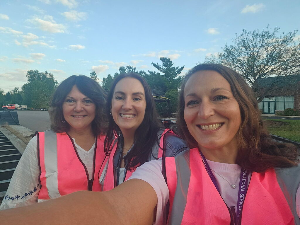 Three women in bright pink safety vests smiling for an outdoor selfie.