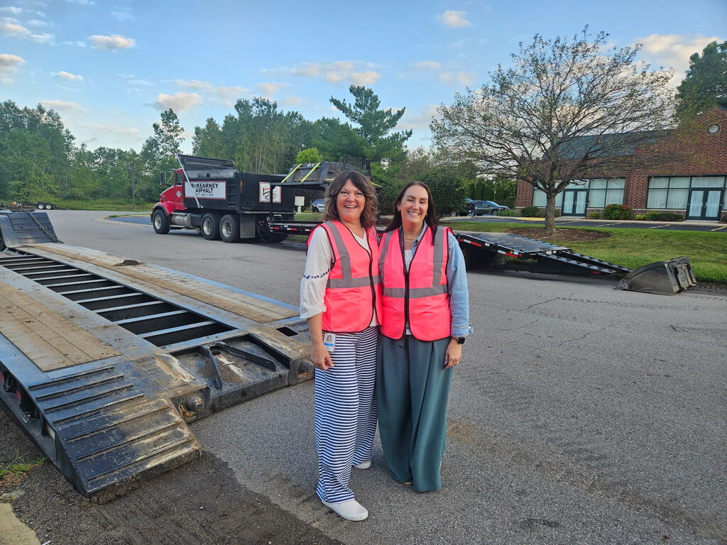 Two women in bright pink safety vests standing outside near construction vehicles.