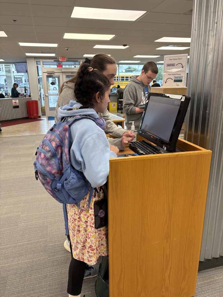 A student and instructor using a computer kiosk indoors.