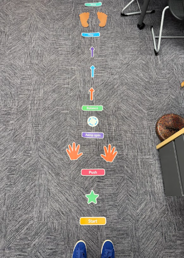 A sensory movement path made of colorful decals laid out in a straight line on a carpet floor, with activity prompts like Start, Push, Jump spin, Balance, and Hop.
