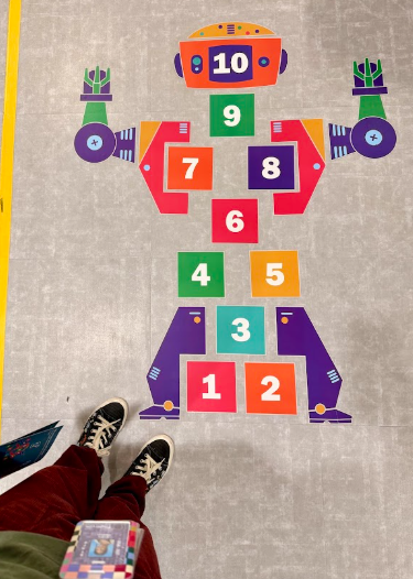 A colorful, robot-shaped hopscotch grid decaled onto a gray tile floor with numbers 1 through 10.