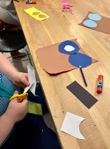 A child using scissors to cut paper at a wooden table during an owl art project