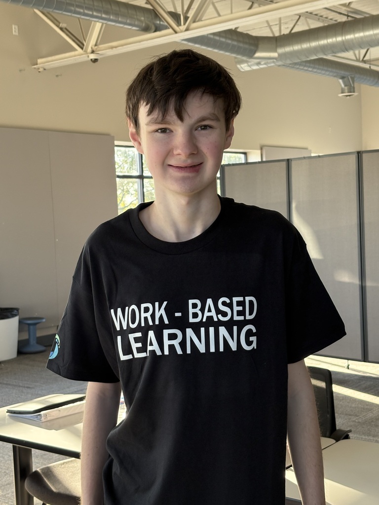 A smiling young man wearing a black t-shirt that reads "WORK - BASED LEARNING".