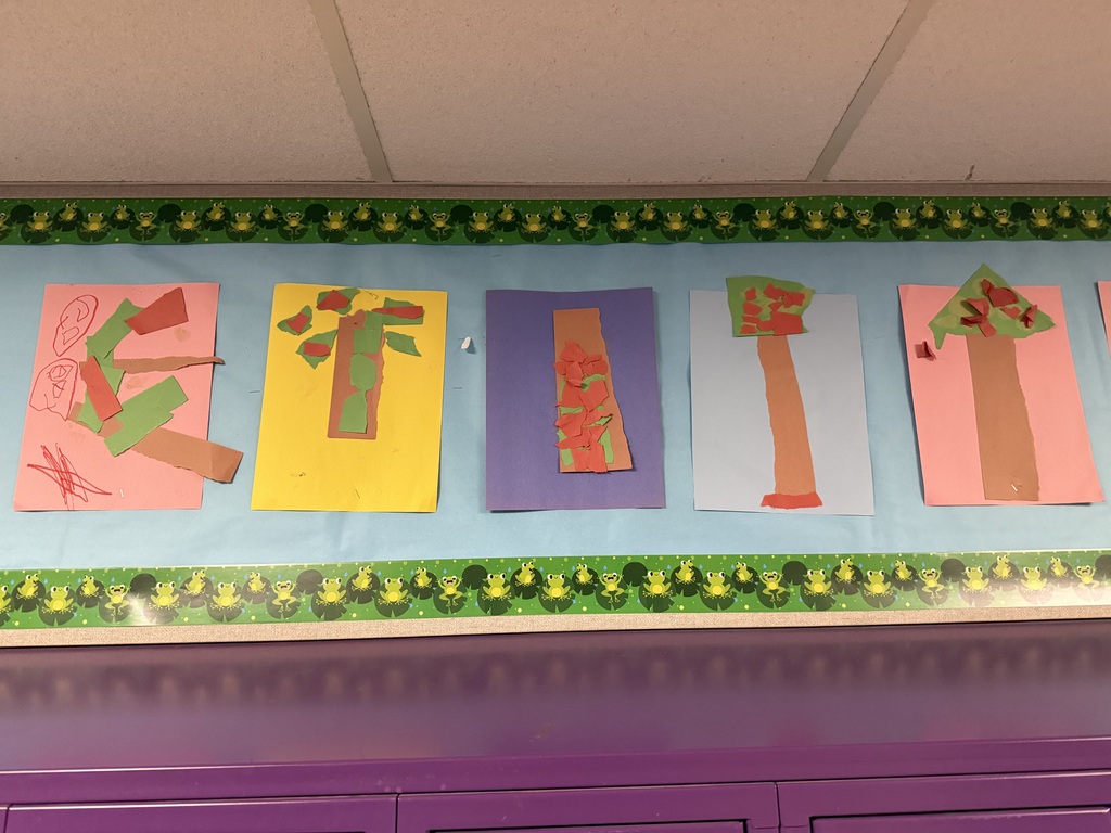 Colorful preschool tree collages made with torn construction paper displayed on a classroom bulletin board above purple cabinets.
