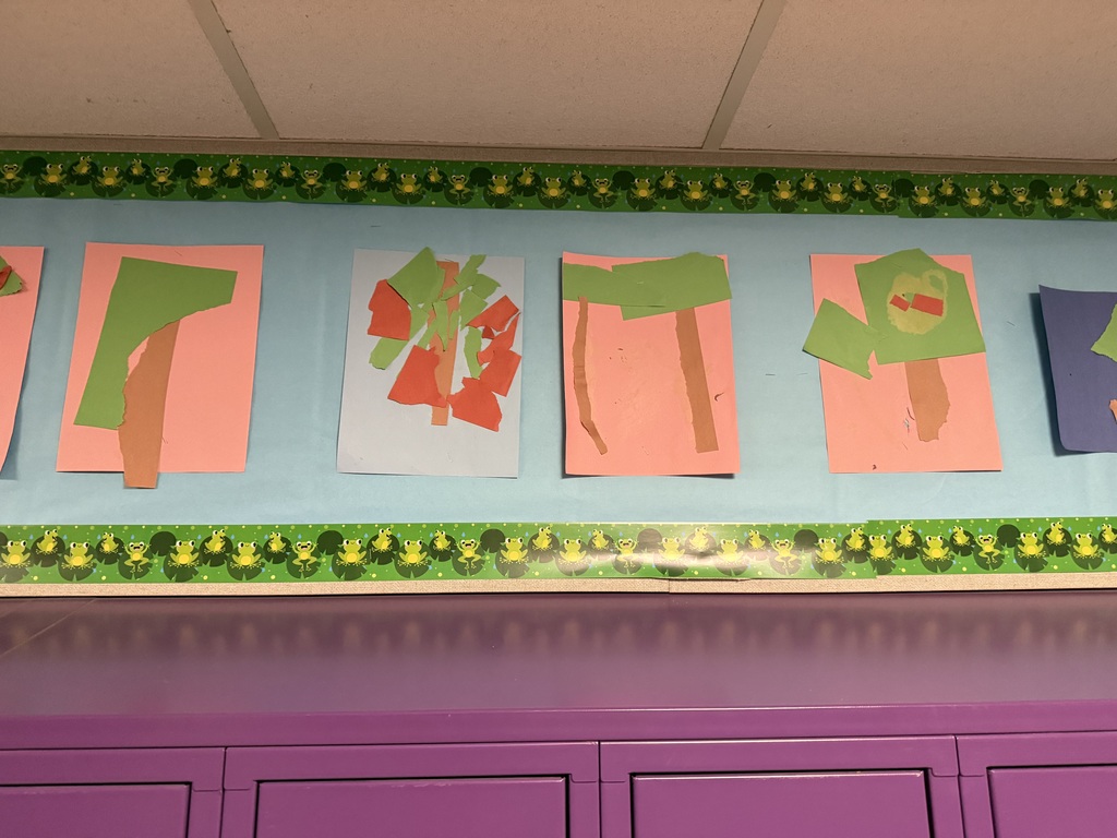 A collection of children's unique tree artwork using green, red, and brown paper pieces on colorful backgrounds, displayed in a preschool classroom.