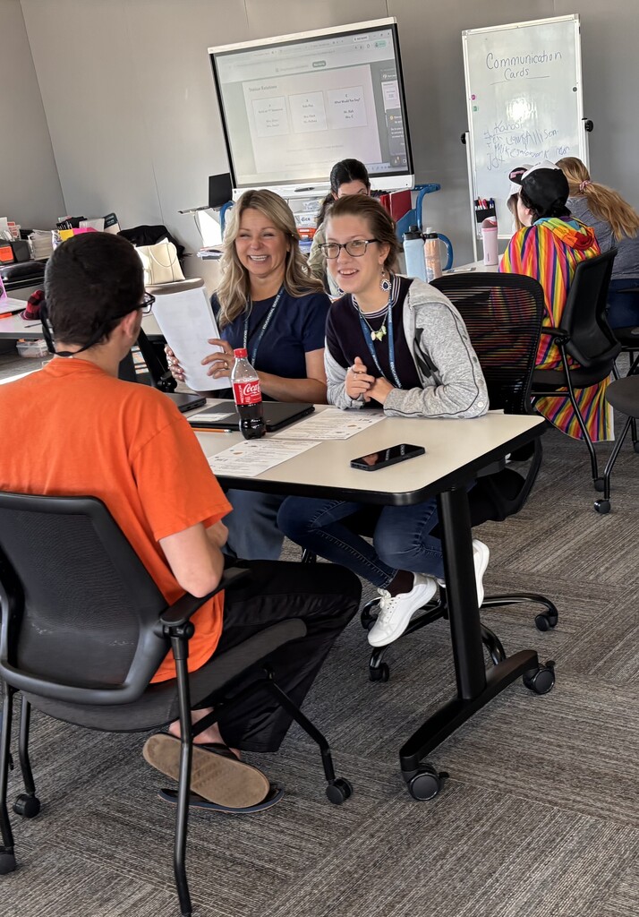 A staff member and a student smiling and talking across a desk during a one-on-one or small group activity.
