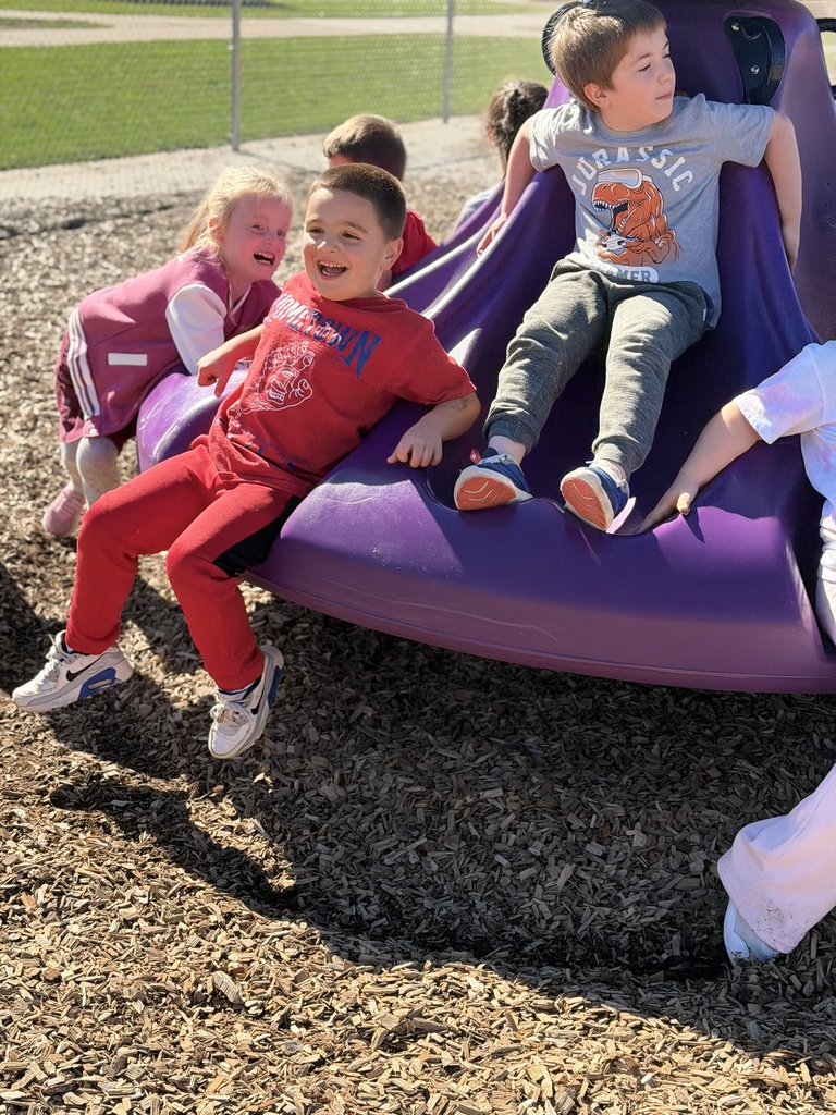 Children smiling and laughing together while playing on a purple playground structure outdoors on a sunny day.