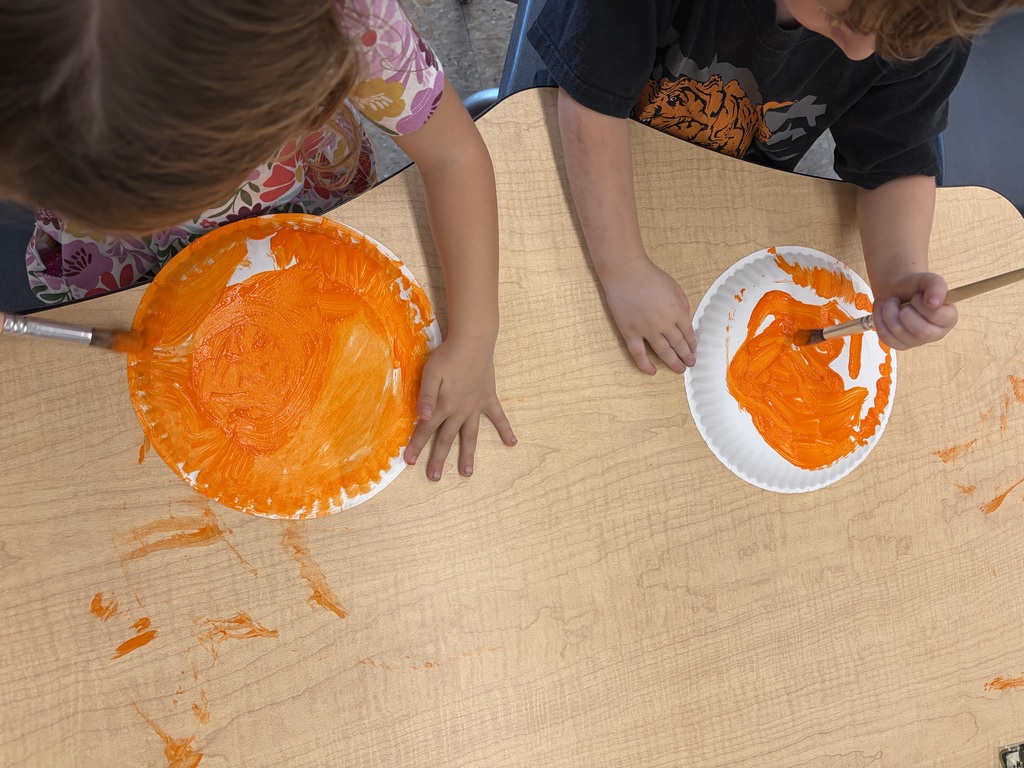 Preschoolers use paintbrushes to cover paper plates with bright orange paint as they create their own pumpkins for fall.