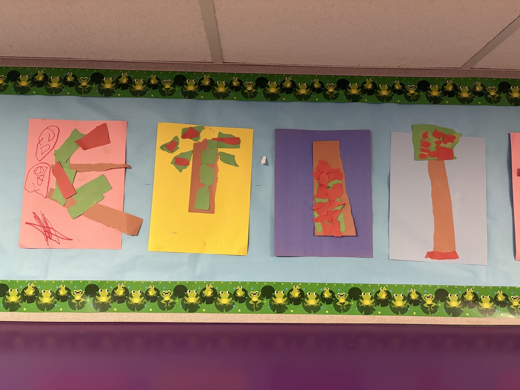 Preschool children’s torn-paper tree art displayed on a classroom bulletin board. The colorful creations feature ripped and layered pieces of green, brown, and orange paper on bright backgrounds, showcasing the children’s creativity while developing fine motor skills through ripping, tearing, and sticking paper.