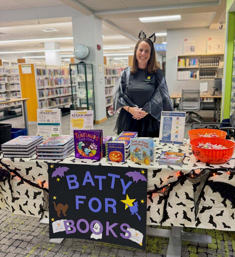 Woman dressed as a bat standing behind a table of books.
