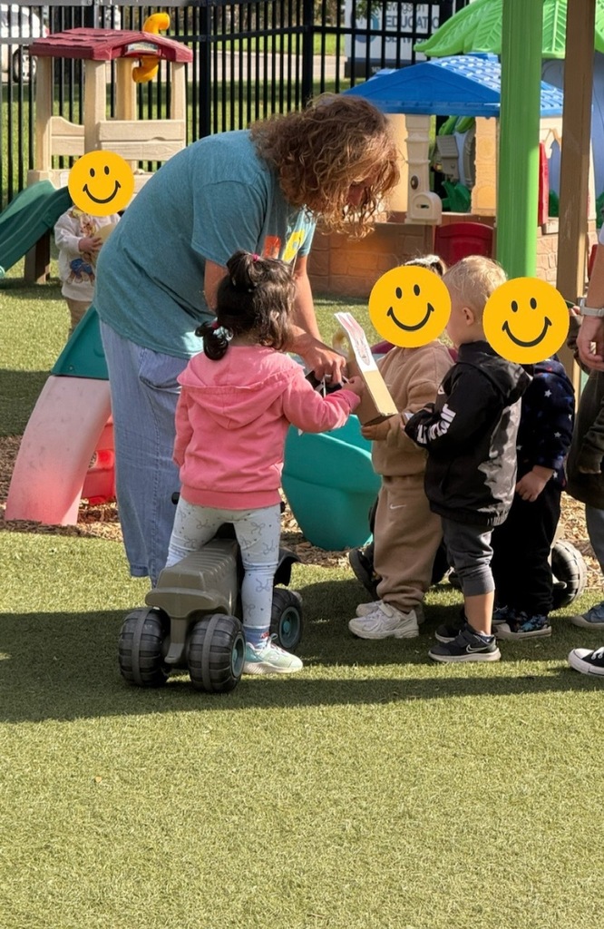 Early Literacy Coach Lisa shares a book with a small group of children gathered around her on an outdoor playground.