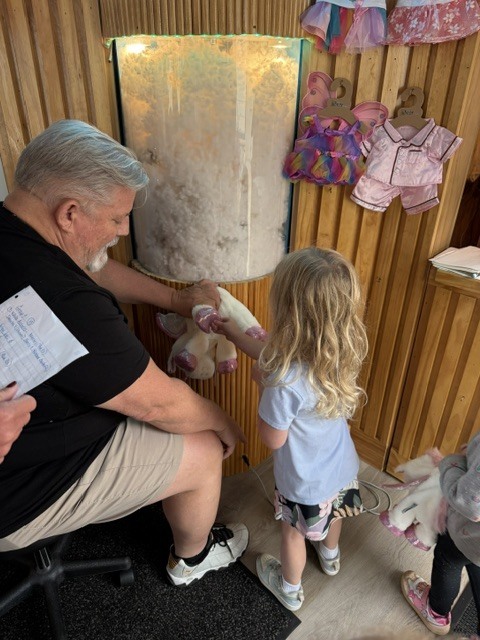 A preschool student works with a Bear Factory staff member to fill a stuffed animal with stuffing.