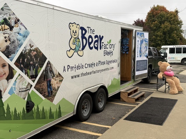 The Bear Factory mobile trailer parked outside the school, with a large teddy bear displayed near the entrance.