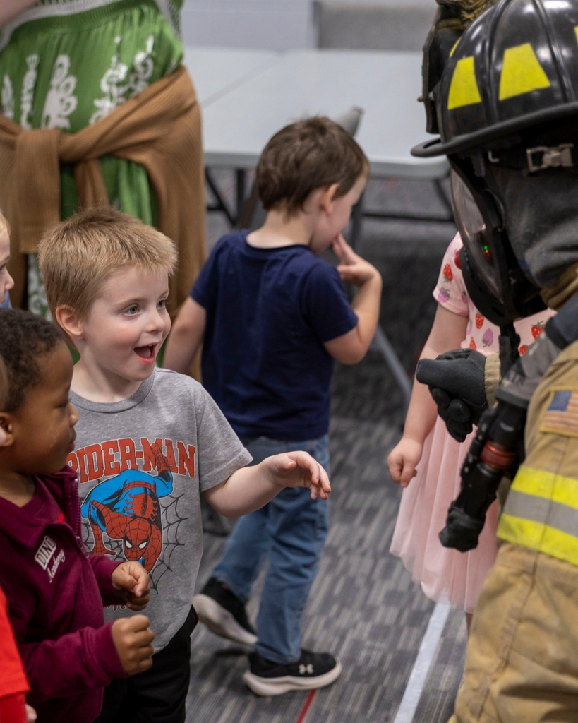 An excited young boy in a Spider-Man shirt high-fives a firefighter in full gear.