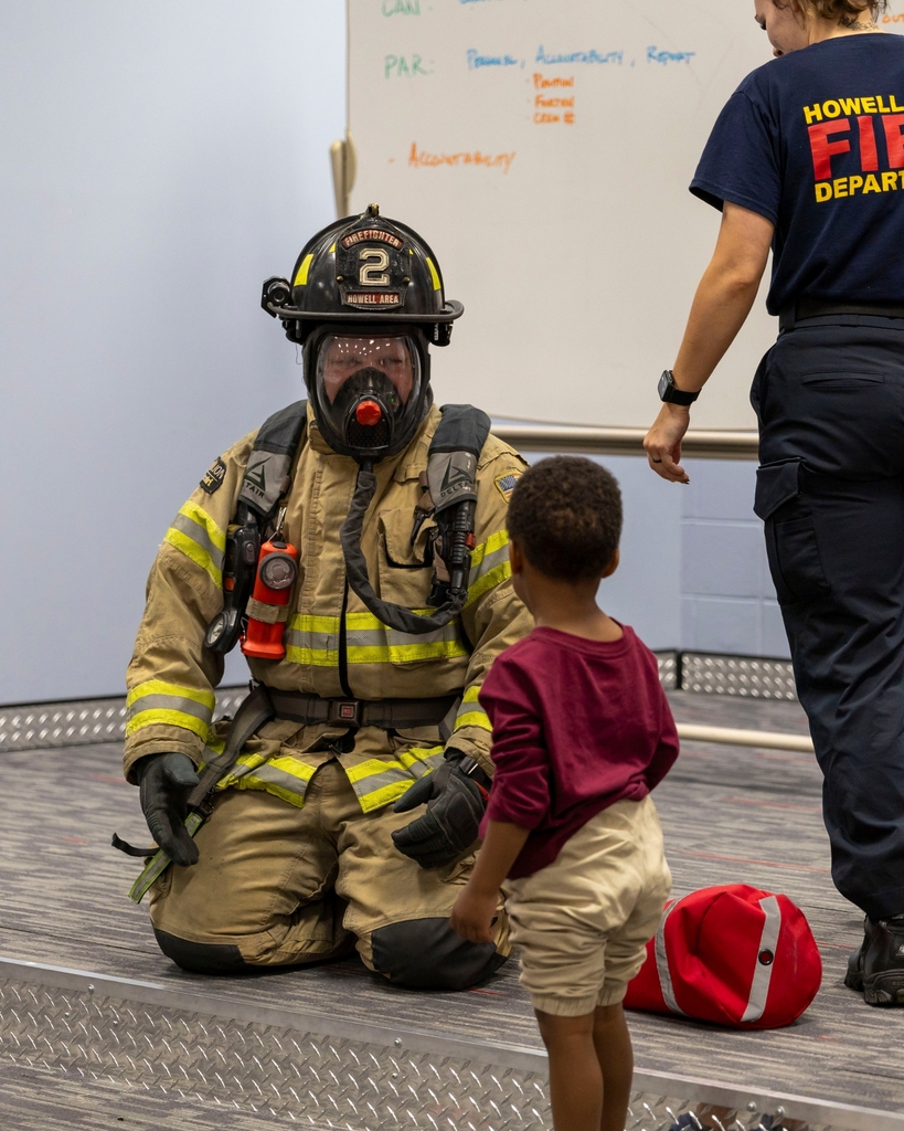 A firefighter in full turnout gear kneels to talk with a young boy.