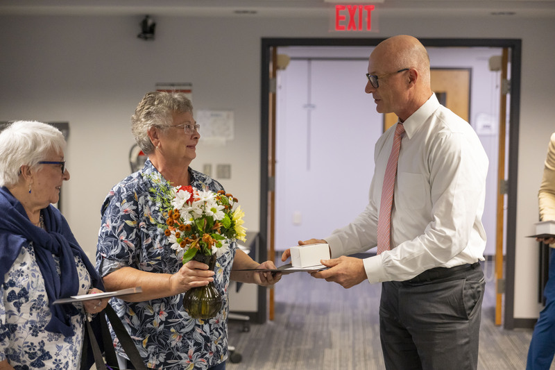 A man in a shirt and tie presents a certificate and gift to a woman holding a flower bouquet.
