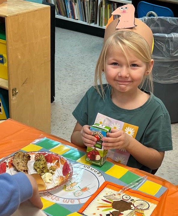 A student with a turkey headband on holds a juicebox.