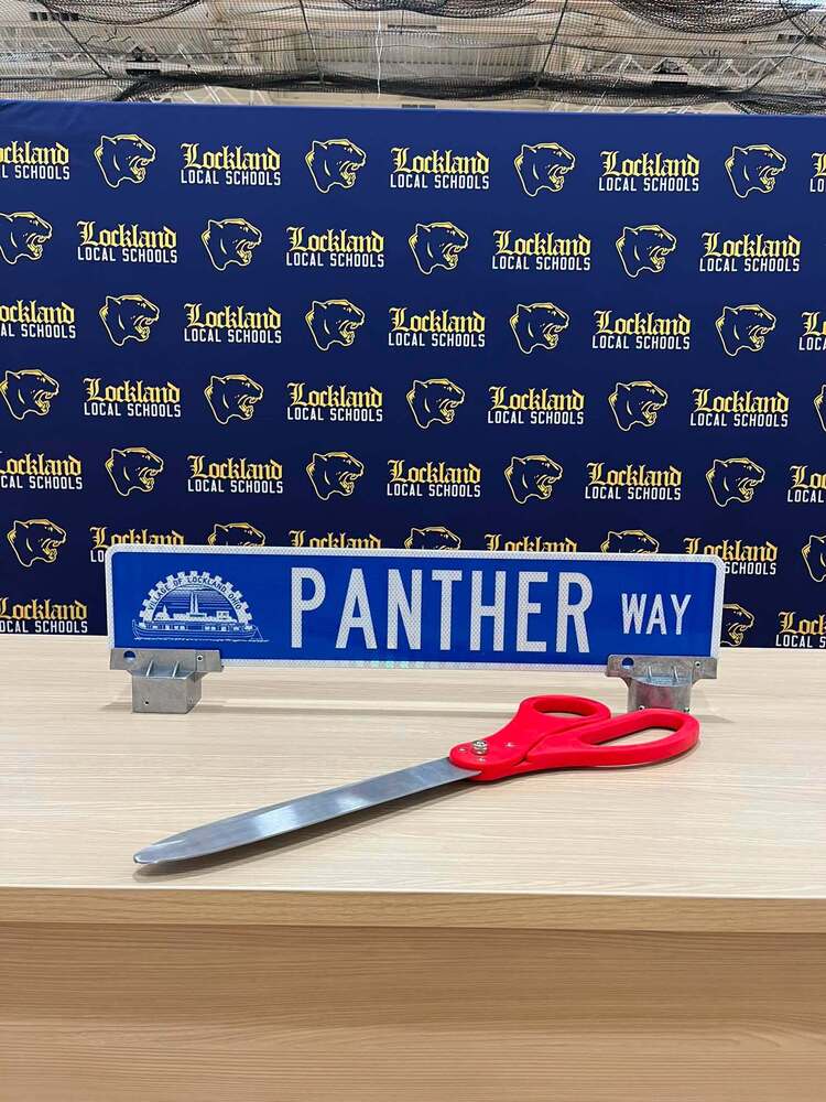 A road sign reading Panther Way and a giant pair of scissors on a table