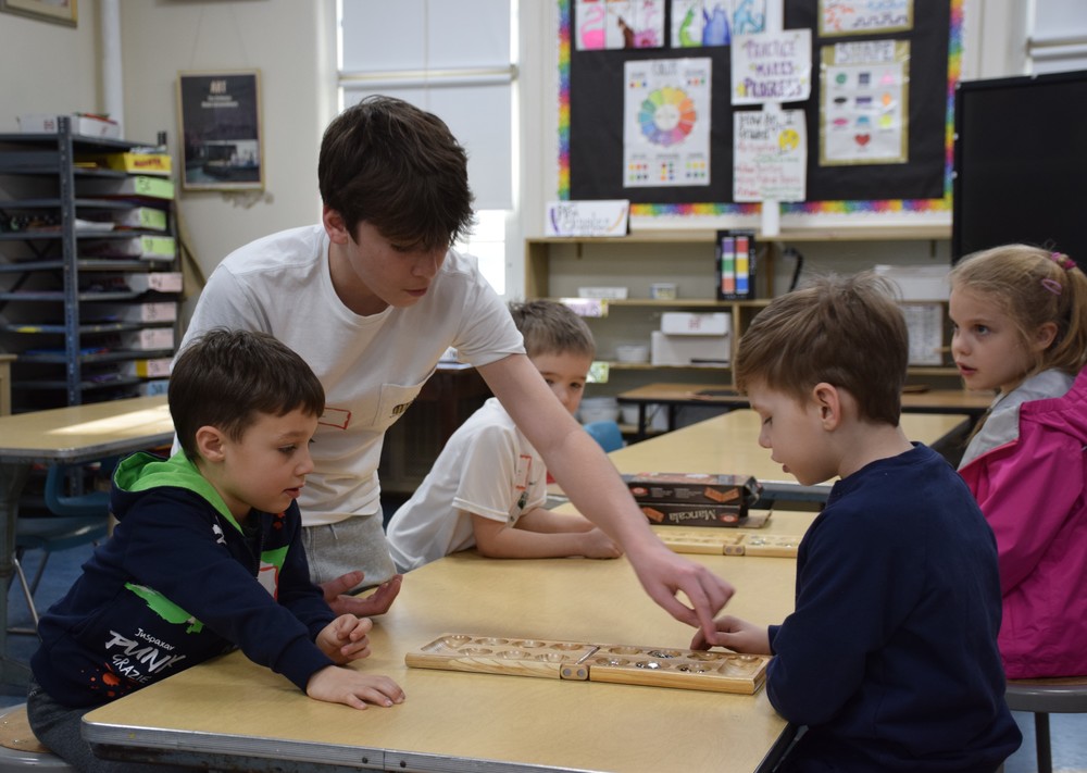 A high school student teaches elementary students how to play a game on Unplugged Night.