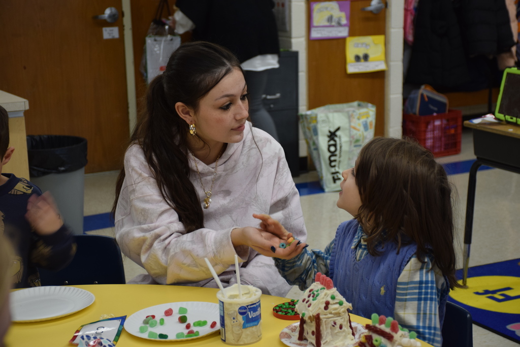 A high school student provides a BP student with candy to place on the gingerbread house.