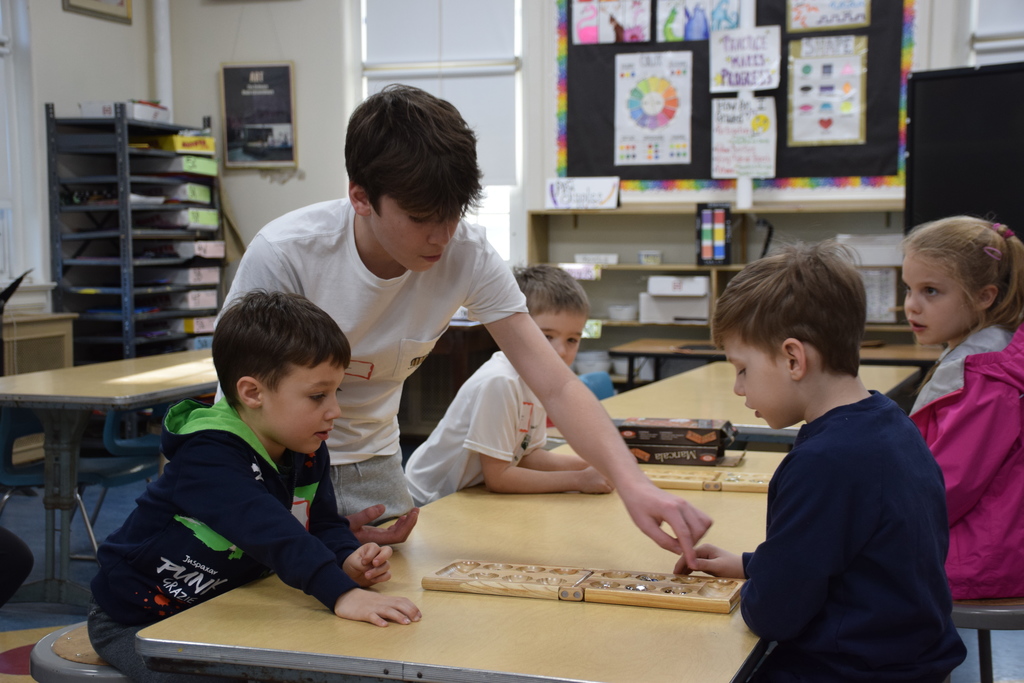A high school student teaches elementary students how to play a game on Unplugged Night.