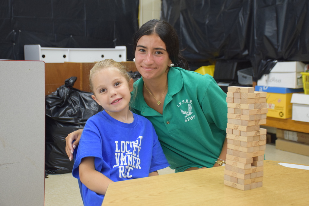 A summer recreation camper and counselor build a jenga tower together.