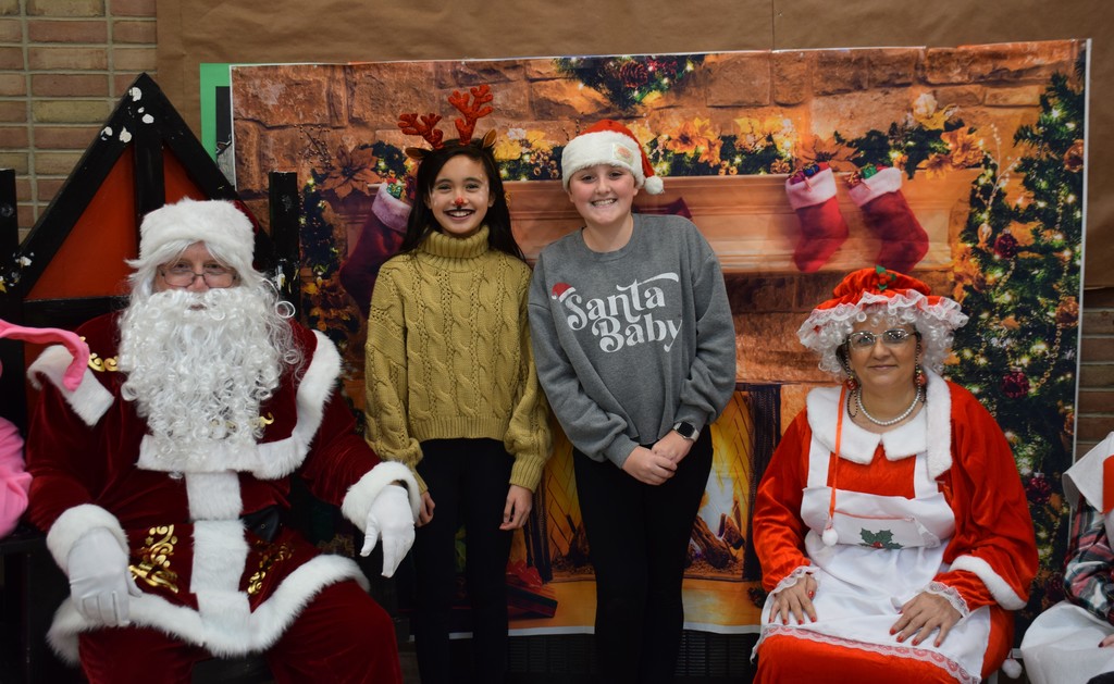 3)	Locust Valley Middle School students Elisa Tan (center left) and Alexandra Stanco (center right) dressed up in holiday gear to meet Santa and Mrs. Claus.