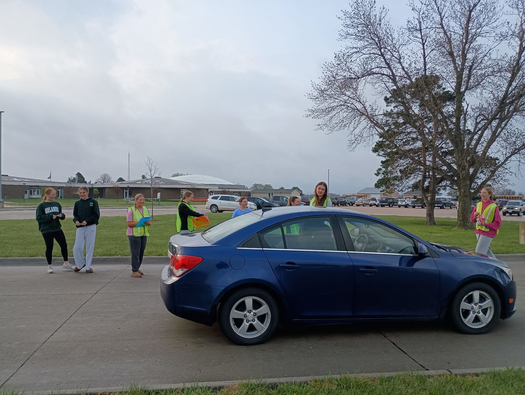 Fccla members handing out Smarties Candy to people wearing seatbelts in blue car at school.