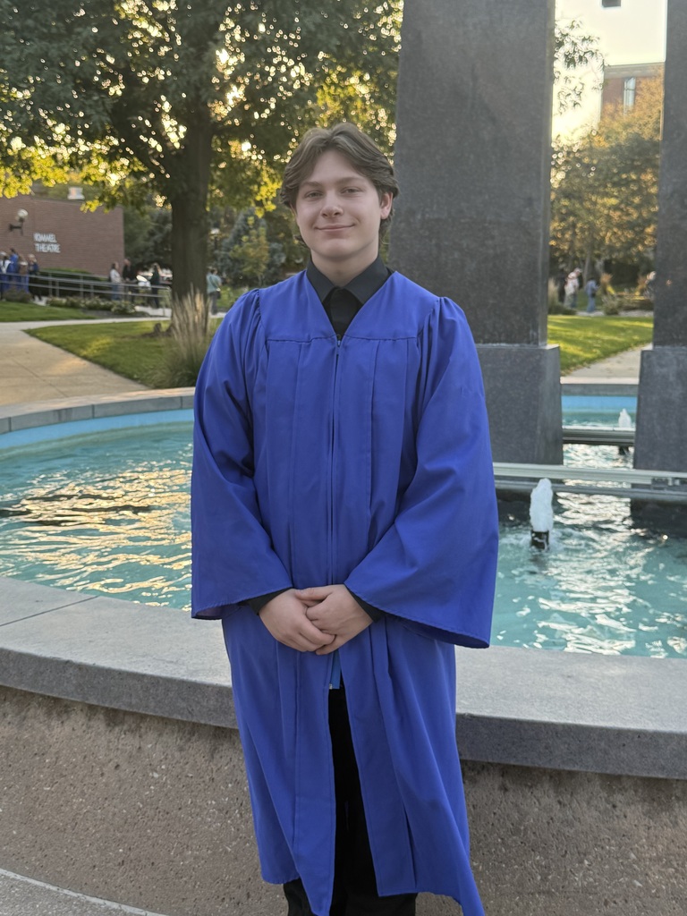 Student in a blue choral robe poses in front of a water display.