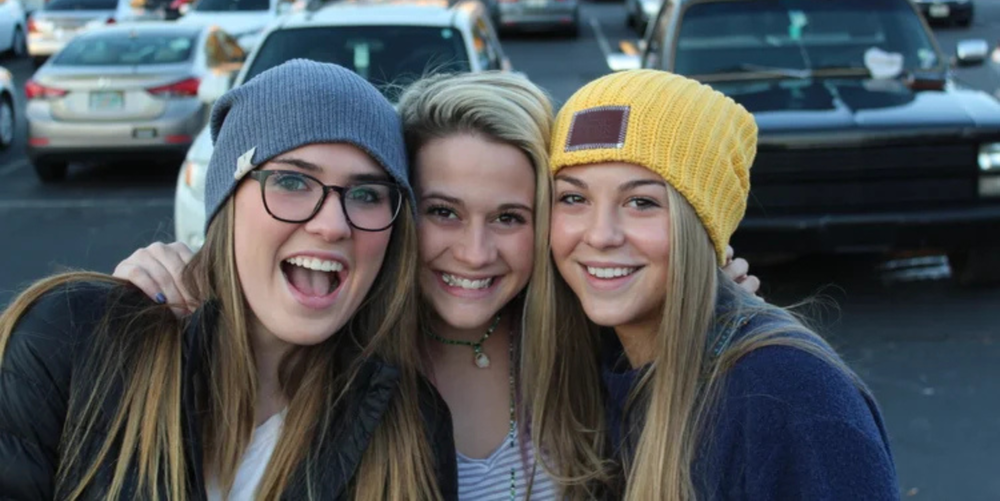 Three high school aged girls pose for a photo smiling. 