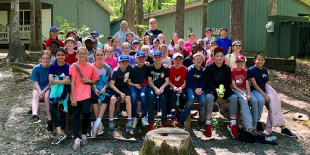 A group of middle school students gather for a group photo smiling while outdoors.