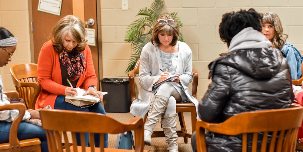 A group of ladies gather in a prayer circle, writing down specific prayers concerning Loganville Christian Academy.