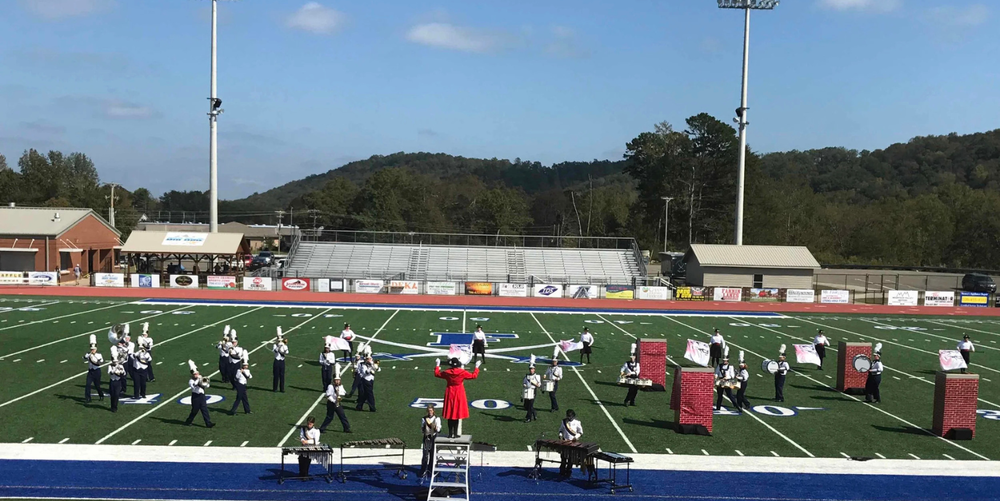 A large group of students wearing band uniforms on a green and blue football field. 